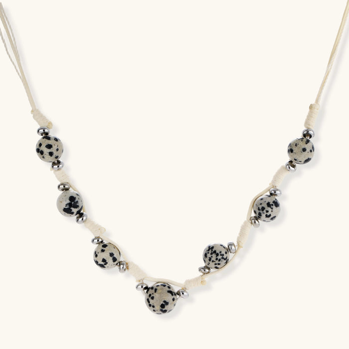 Adjustable cream cord necklace with white spotted stone beads featuring black speckles on neutral background