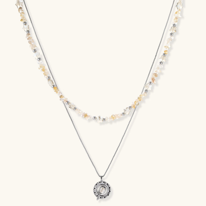 Two-layer necklace with natural stone chips and eco-brass beads, featuring a circular wrapped pendant on cream background.