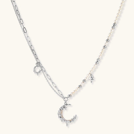 Silver-toned crescent moon pendant with star accents on pearl and chain necklace against white background.