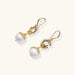 Gold sunburst charm earrings with baroque pearl drops on French hooks against cream background