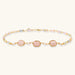 Gold necklace with three rose quartz stones, multicolor pastel beads, and pearl accents on white background.