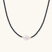 Delicate necklace with black blue sandstone beads and baroque pearl center on white background with gold accents.