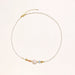 Delicate white beaded necklace with baroque pearl center, gold accents, and coral and aqua gemstones on cream background.