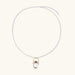 Whimsical owl pendant holding a white pearl on a gold swing, rhodium-plated silver chain on cream background.