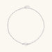 Dainty rhodium-plated silver chain necklace with centered 10mm freshwater pearl and crystal accents on cream background