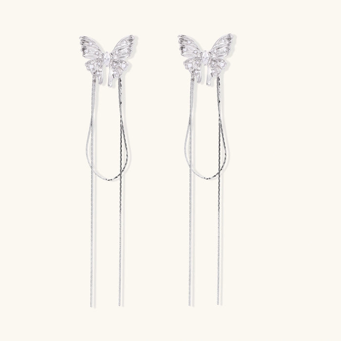 Pair of silver threader earrings with crystal butterfly tops and long chain drops on cream background.