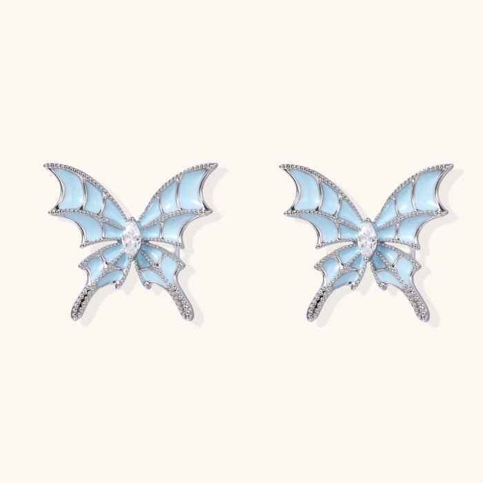 Long silver-tone earrings with powder blue enamel butterfly studs and flowing chain tassels on cream background
