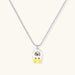 Chrome egg-shaped pendant with kawaii face, yellow bow, and pearl detail on silver chain against white background