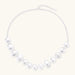 Graduated pearl-finish silver discs forming an organic bubble bib necklace on delicate chain against cream background.