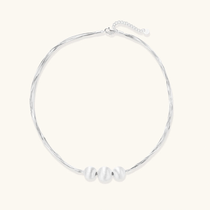 Sterling silver multi-strand necklace with three brushed round beads on cream background