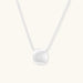Minimalist brushed sterling silver dome pendant on delicate chain against cream background, showing matte textured finish