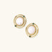 Circular gold stud earrings with iridescent mother-of-pearl center and green zirconia accents on cream background.