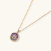 Gold-plated circular pendant with hand-painted purple enamel floral design on delicate chain against cream background