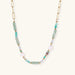 Gold chain necklace with seafoam green quartz cylinders, turquoise beads, and baroque pearl on cream background