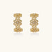 Gold hoop earrings with intricate three-dimensional floral filigree pattern in 14K gold plated brass on cream background