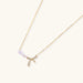Delicate gold necklace with three white pearls and crystal-embellished bow pendant on cream background
