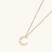 Gold crescent moon pendant with graduated white pearls on delicate chain against cream background