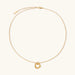 Delicate gold-plated necklace with three interlocking circle rings forming a minimalist knot pendant on cream background
