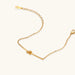 Delicate gold chain bracelet with minimalist bar and centered knot detail on cream background