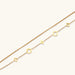 Double-layer gold-plated bracelet with quatrefoil and star charms on cream background, 18K gold finish.