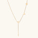 Gold Y-shaped necklace with L-O-V-E letter charms and vertical bar pendant on delicate chain against cream background