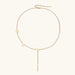 Gold Y-shaped necklace with L-O-V-E letter charms and vertical bar pendant on delicate chain against cream background