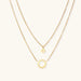 Gold layered necklace set with sunburst and smiley face pendants on delicate chains against white background.