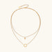 Gold layered necklace set with sunburst and smiley face pendants on delicate chains against white background.