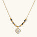 Gold-toned beaded necklace with grey stones and quatrefoil abalone shell pendant on cream background.