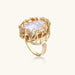 Gold filigree crown ring cradling an iridescent baroque freshwater pearl with crystal accents on white background